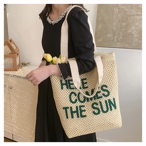 Detail of woven straw tote bag with Here Comes The Sun green embroidery text
