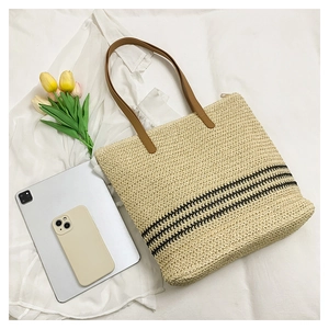 Close-up of handwoven straw tote with black stripes and brown leather handles on white fabric