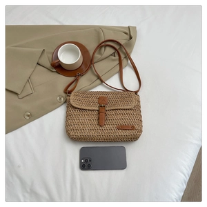 Detail view of woven straw crossbody bag with leather strap next to a mobile phone