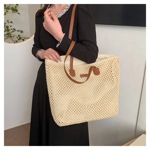 Detail of hand-woven straw tote bag showing beige mesh texture and brown leather strap