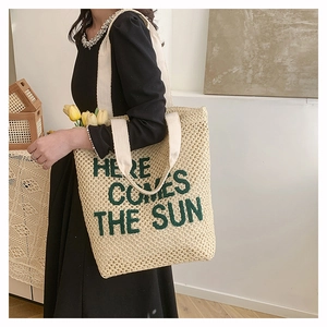 Detail of crochet tote bag featuring green Here Comes The Sun text on off-white fabric