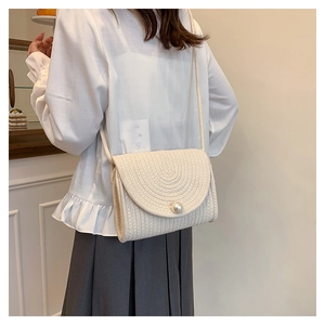 Detail view of cream woven straw crossbody bag with pearl closure worn by a model