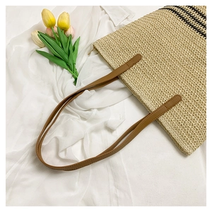 Close-up of beige straw woven tote bag with black stripes and brown leather handles