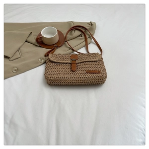Detailed view of woven straw bag with brown leather strap and decorative buckle