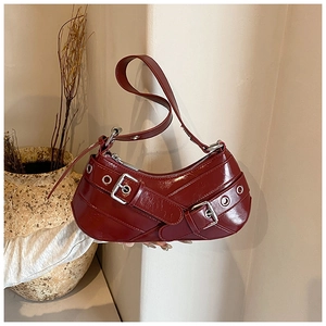 Detail view of burgundy crescent shoulder bag with silver eyelet buckles and glossy texture