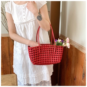 Detail of red hollow woven tote bag held by a model in a warm rustic setting