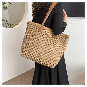 Detailed view of the large straw tote bag with brown leather straps worn by a model