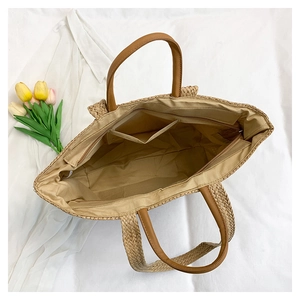 Detailed interior of a straw tote bag with zipper pocket and brown leather handles