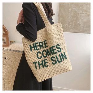 Detail of beige woven tote bag with green Here Comes The Sun embroidery on fine straw texture