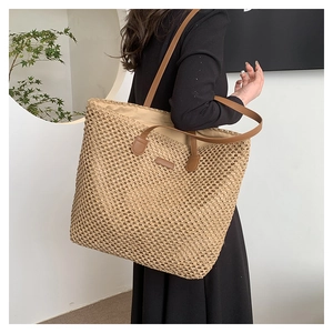 Detail of woven straw tote bag featuring brown leather straps and mesh pattern texture