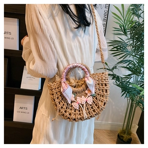 Detail view of woven straw bag with floral charm and decorative pink silk scarf handle
