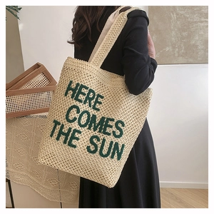 Detail of woven straw tote bag with green Here Comes The Sun text on model
