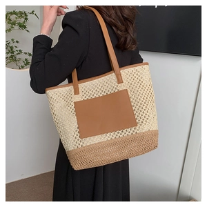 Detail shot of woven paper straw tote bag with brown leather patch and shoulder strap