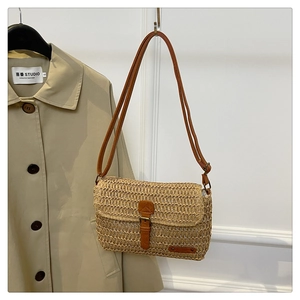 Close-up of woven straw shoulder bag with brown leather strap and buckle on trench coat