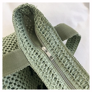 Detail of silver zipper closure and woven texture on a sage green straw tote bag