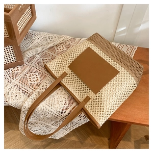 Detail of paper straw woven tote bag with brown leather patch and thin shoulder strap