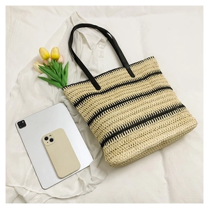 Close-up of woven straw tote bag with black leather handles on a white fabric backdrop