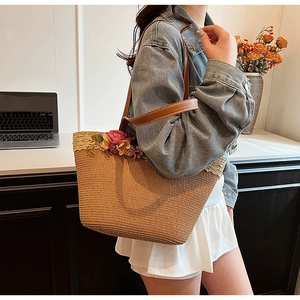 Detailed shot of straw woven tote bag featuring floral accents and brown leather straps