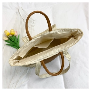 Detailed interior of summer straw tote bag with beige lining, zipper, and brown leather handles