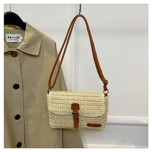Detail of beige straw crossbody bag with brown leather strap and decorative buckle