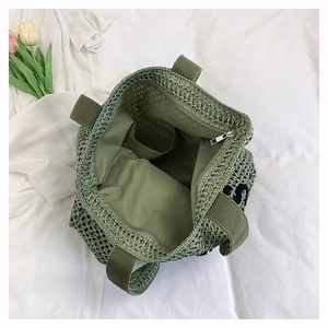 Detail view of woven straw tote bag with zipper closure, inner lining and green mesh texture