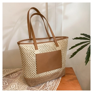 Detail of hollow woven paper straw tote bag with brown leather pocket and long shoulder straps