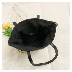 Detail view of woven straw tote bag featuring black fabric lining and golden metal zipper