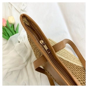 Detail view of woven paper rope straw beach bag with leather trim and metal zipper closure