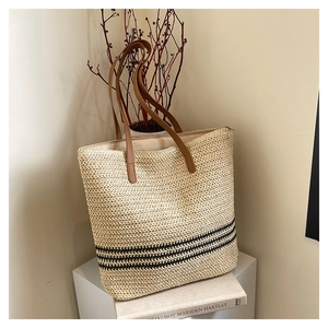 Detail of hand-woven straw tote bag showing black stripes and brown leather straps