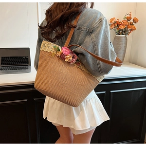 Detail of hand-woven straw tote bag with 3D pink flowers and brown leather shoulder strap