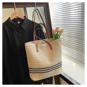 Detail of hand-woven straw tote bag with black stripes and brown leather handles