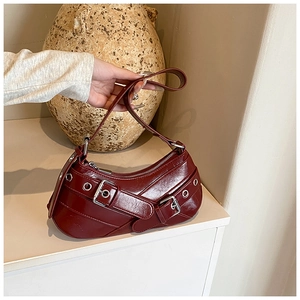 Close-up of wine red glossy leather underarm bag with silver buckles and metal eyelets