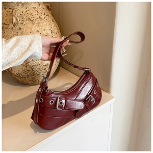 Detail of dark red glossy leather underarm bag with decorative metal eyelet buckle straps