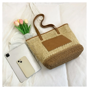Detail of paper straw woven tote bag featuring hollow-out design and brown leather handles
