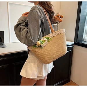 Detail of straw tote bag with white lace trim, floral accents and leather shoulder strap