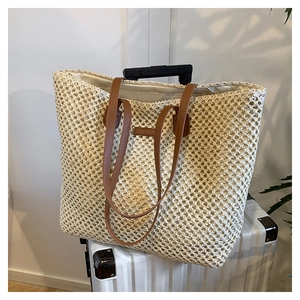 Fashionable beige straw woven tote bag with brown leather handles on a suitcase