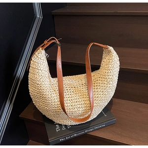 Close-up of beige woven straw hobo bag with adjustable brown leather strap on books
