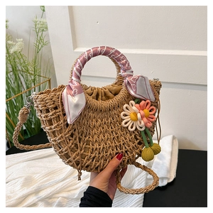Detailed close-up of straw woven handbag with floral accents and silk scarf handle decor