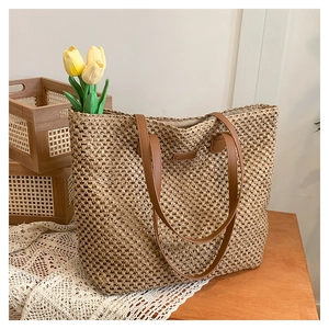 Large straw tote bag with brown leather handles and natural woven texture on a wooden table