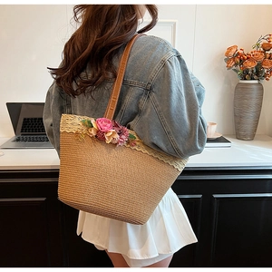 Detail of straw tote bag with delicate lace trim, purple floral decor and leather handle