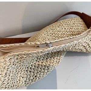 Detail of crochet straw tote bag showing zipper closure and brown leather strap texture
