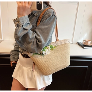 Detail of straw tote bag with white lace trim and floral accents on slim brown straps