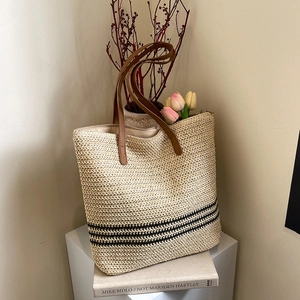 Handwoven straw tote bag with black stripes and brown leather handles for summer beach