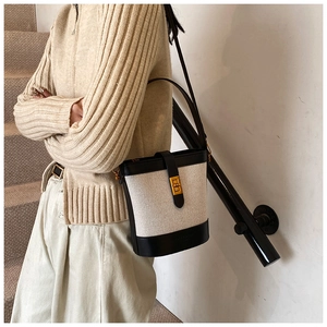 Sac seau en toile crème avec finitions en cuir noir porté à l'épaule sur un pull