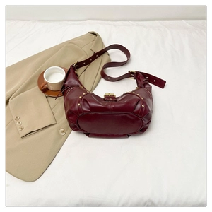 Gros plan du sac demi-lune bordeaux avec rivets dorés sur un tissu blanc