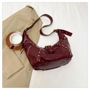 Détail du sac demi-lune bordeaux avec rivets dorés sur fond de tissu blanc doux