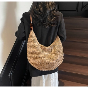 Detail of a large woven straw crescent bag with a dark brown leather adjustable strap