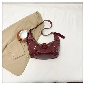 Détail du sac croissant bordeaux avec rivets métalliques et boucles sur tissu blanc
