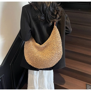 Rear view of a model carrying a large straw crescent tote bag with brown leather strap