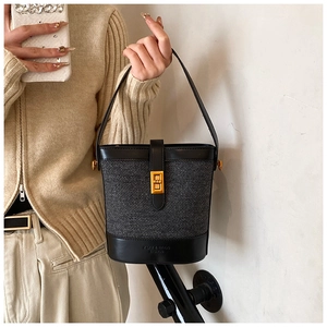 Détail du sac seau tissé gris avec bordure en cuir noir et fermoir rotatif doré élégant